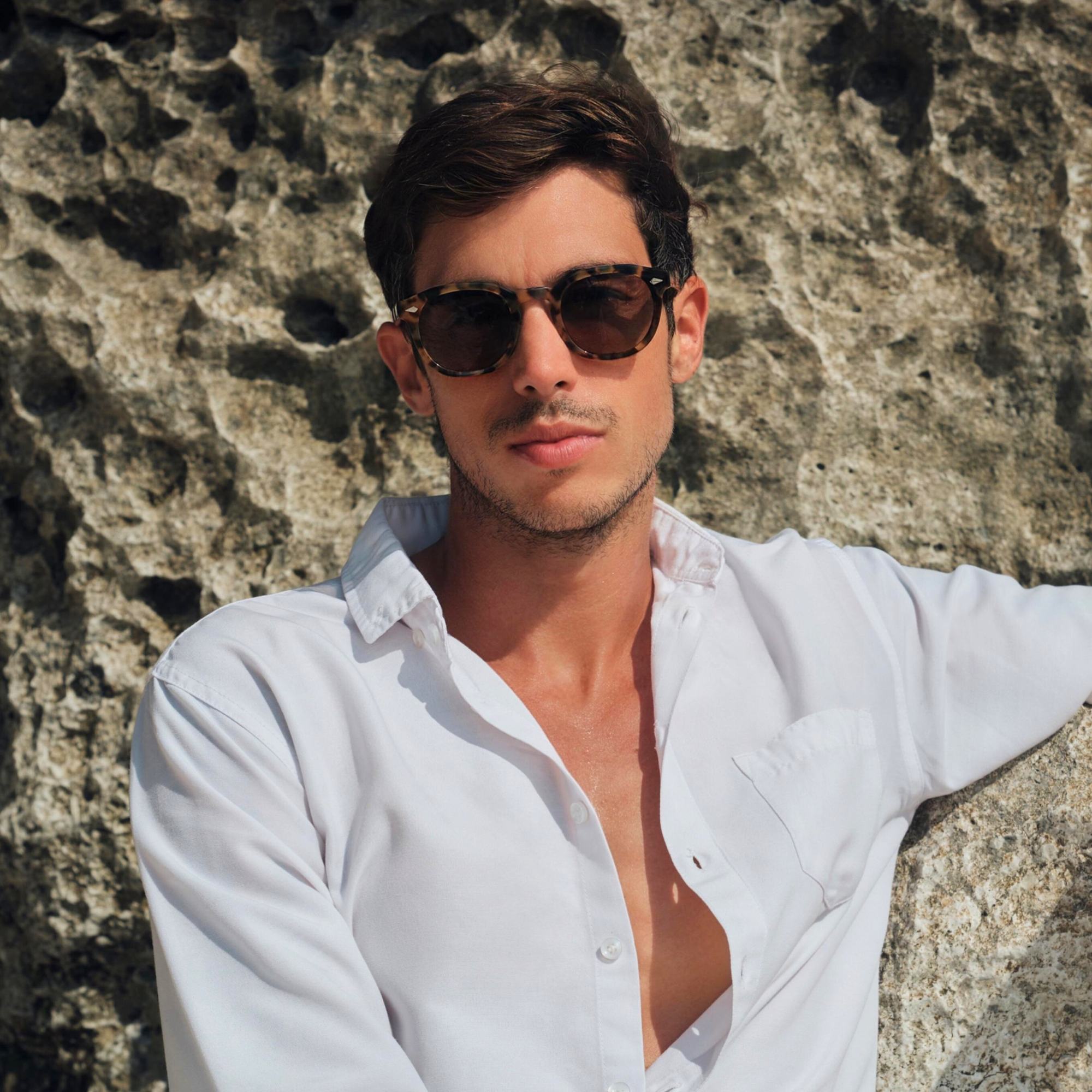 Man wearing sunglasses and a white shirt against a stone wall